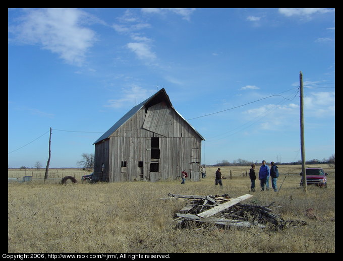 100 year old barn with brown dry grass near by. The large door the the hay loft is hanging crooked and looks like it could fall.